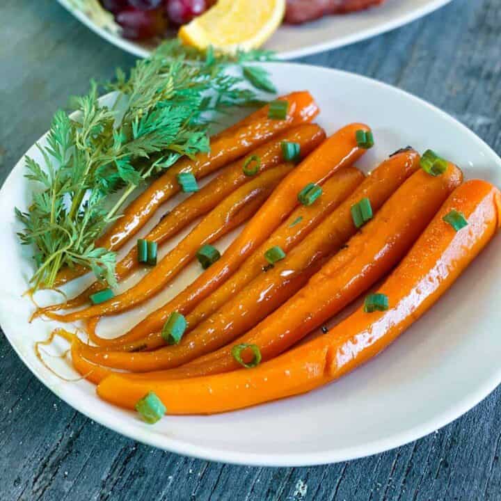 Candied carrots on a white plate with fresh herbs and green onions