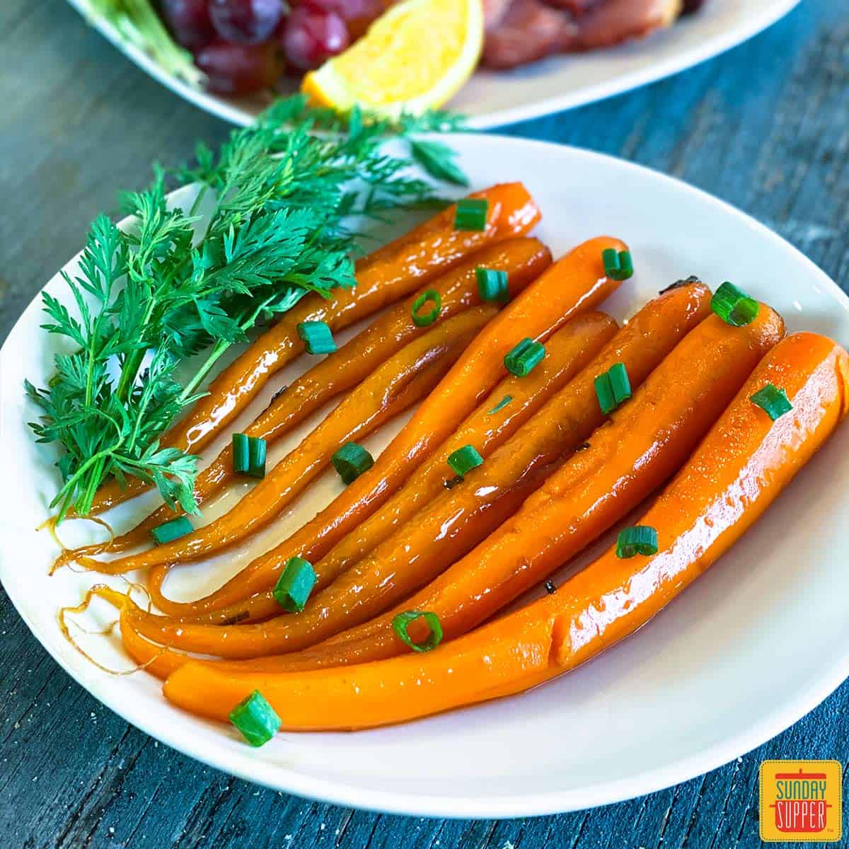 Candied carrots on a white plate with green onions and fresh herbs