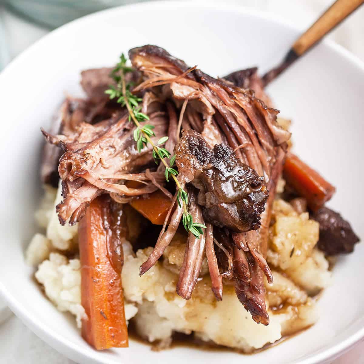 Close up of dutch oven pot roast in a white bowl with a fresh sprig of rosemary on top