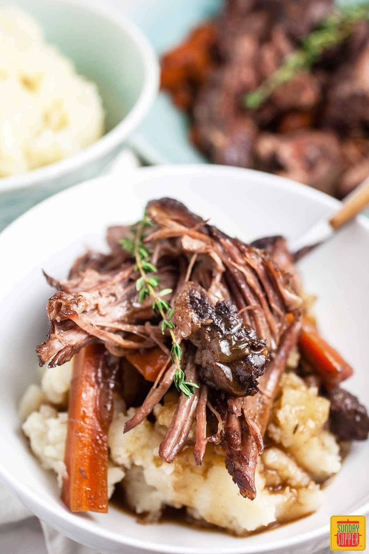 Dutch oven pot roast over mashed potatoes in a white dish