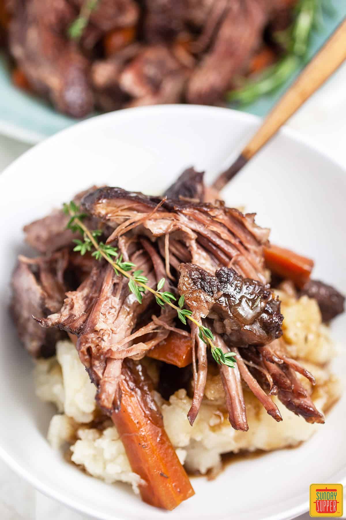 Dutch oven pot roast in a white bowl with a fork and a freesh sprig of rosemary