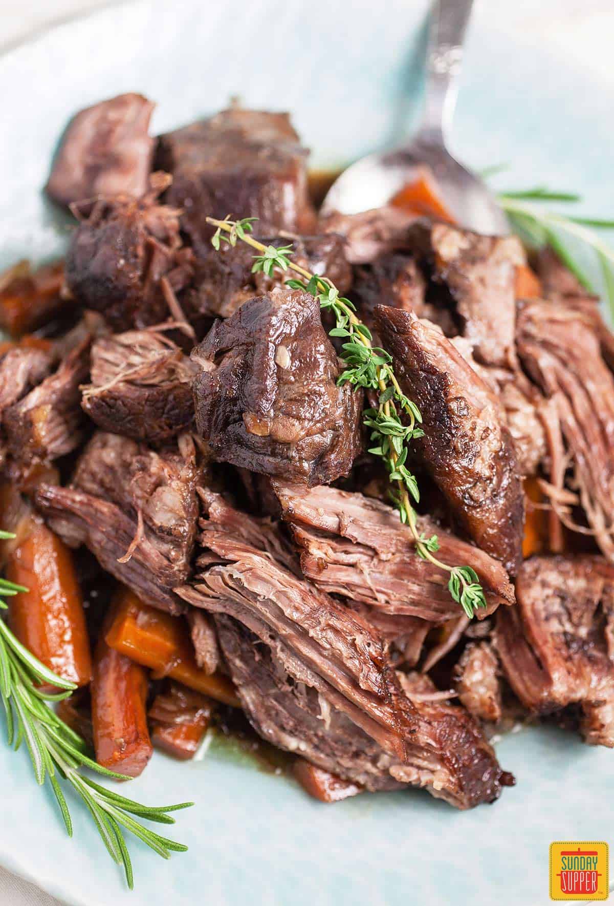 Dutch oven pot roast on a light blue plate with fresh herbs