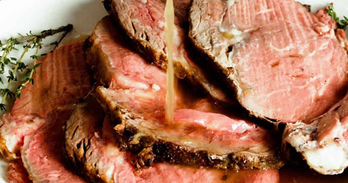 Au jus drizzling over slices of prime rib on a plate
