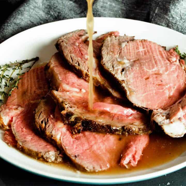 Au jus drizzling over slices of prime rib on a plate