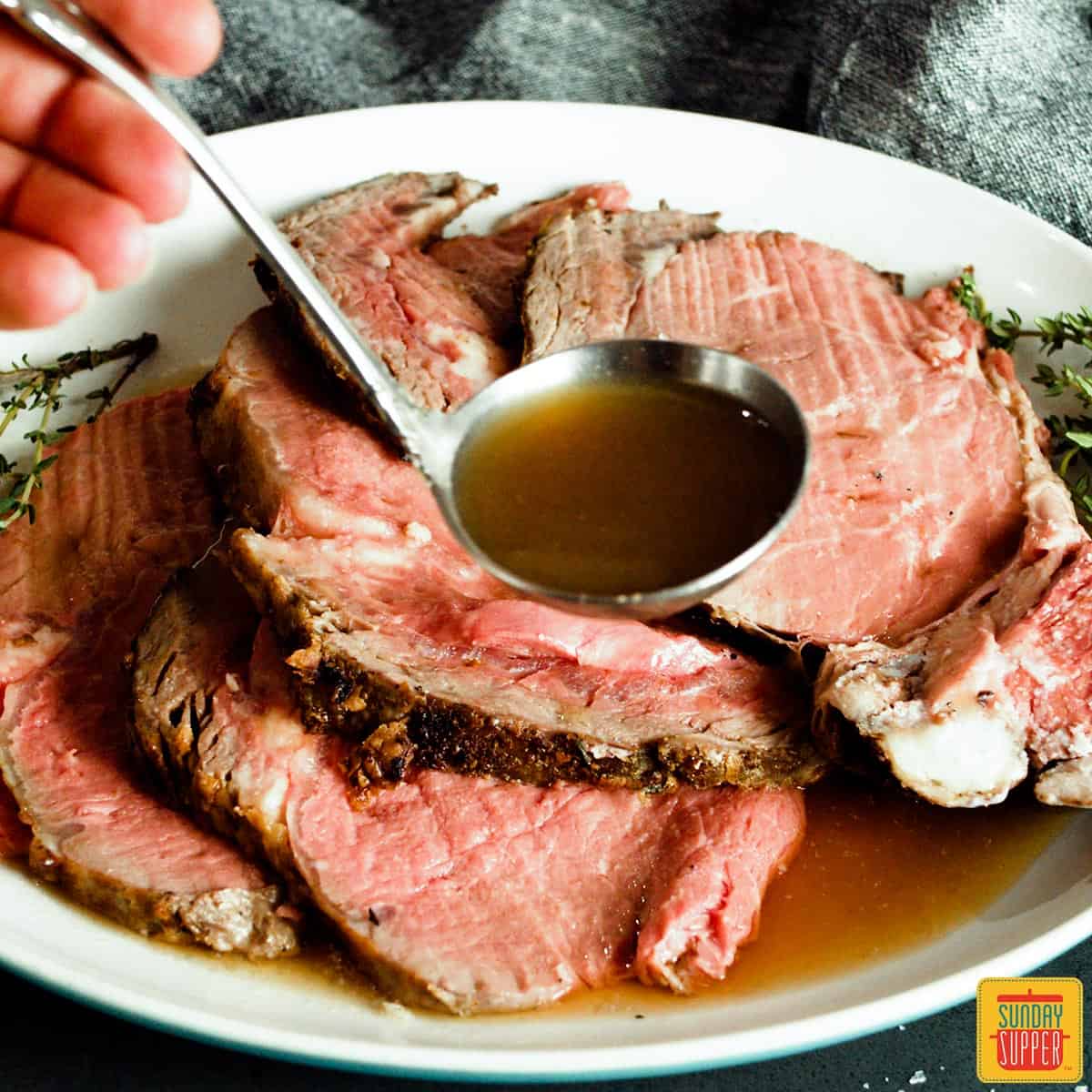 Pouring au jus over slices of prime rib on a white plate