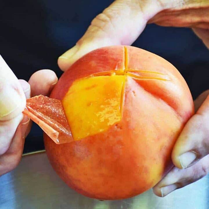 Peeling the skin off a scored peach easily with fingers