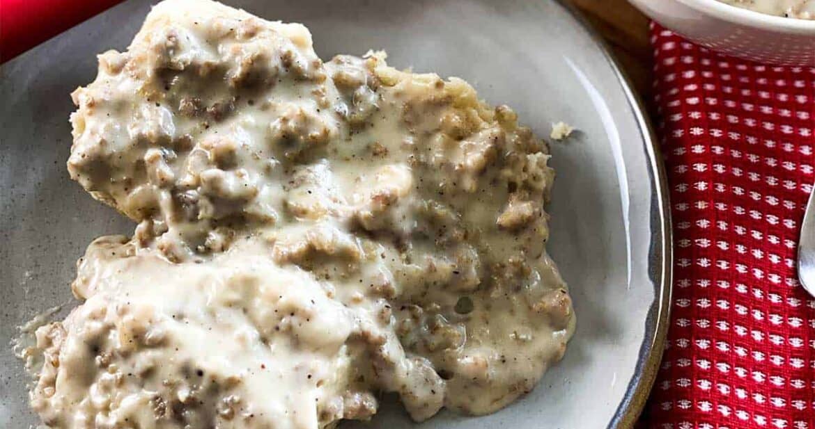 Close up of instant pot sausage gravy on top of biscuits on a plate next to a red spatula