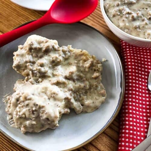 Close up of instant pot sausage gravy on top of biscuits on a plate next to a red spatula