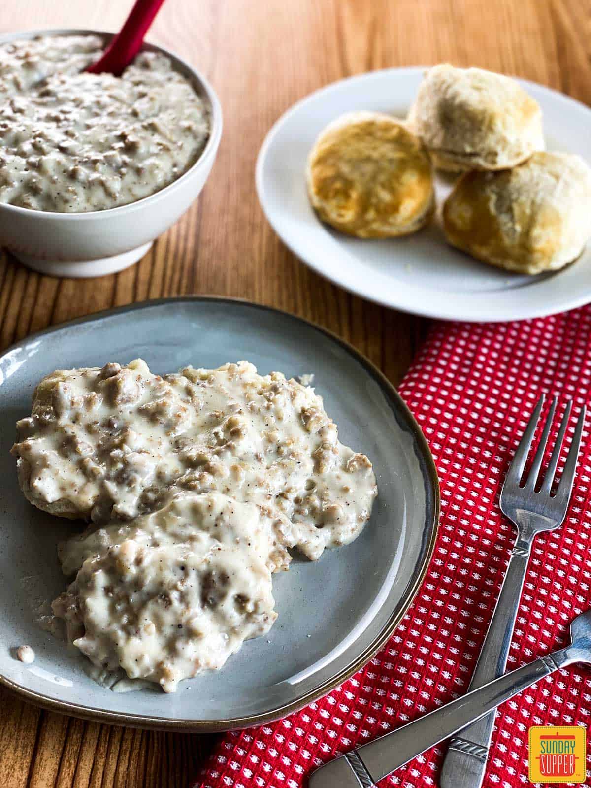 Instant pot sausage gravy served over biscuits next to a plate of biscuits and bowl of gravy