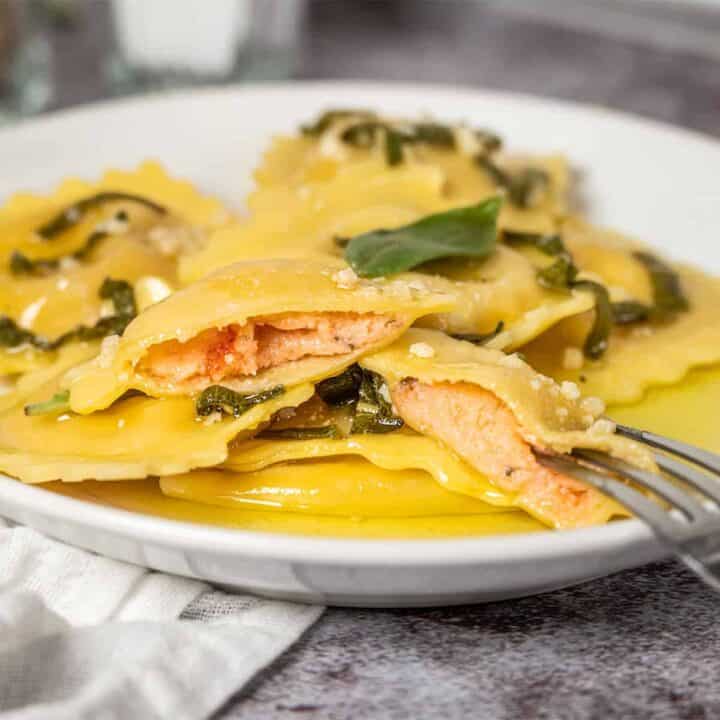 Lobster ravioli on a white plate with one ravioli split open to show the inside