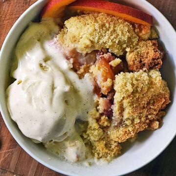 Peach cobbler with ice cream and fresh peach slices in a white bowl