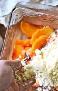 Pouring cake mix crumbs with butter over the top of peaches in a baking dish