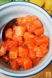 Salmon marinating in poke bowl sauce with a spoon to the side
