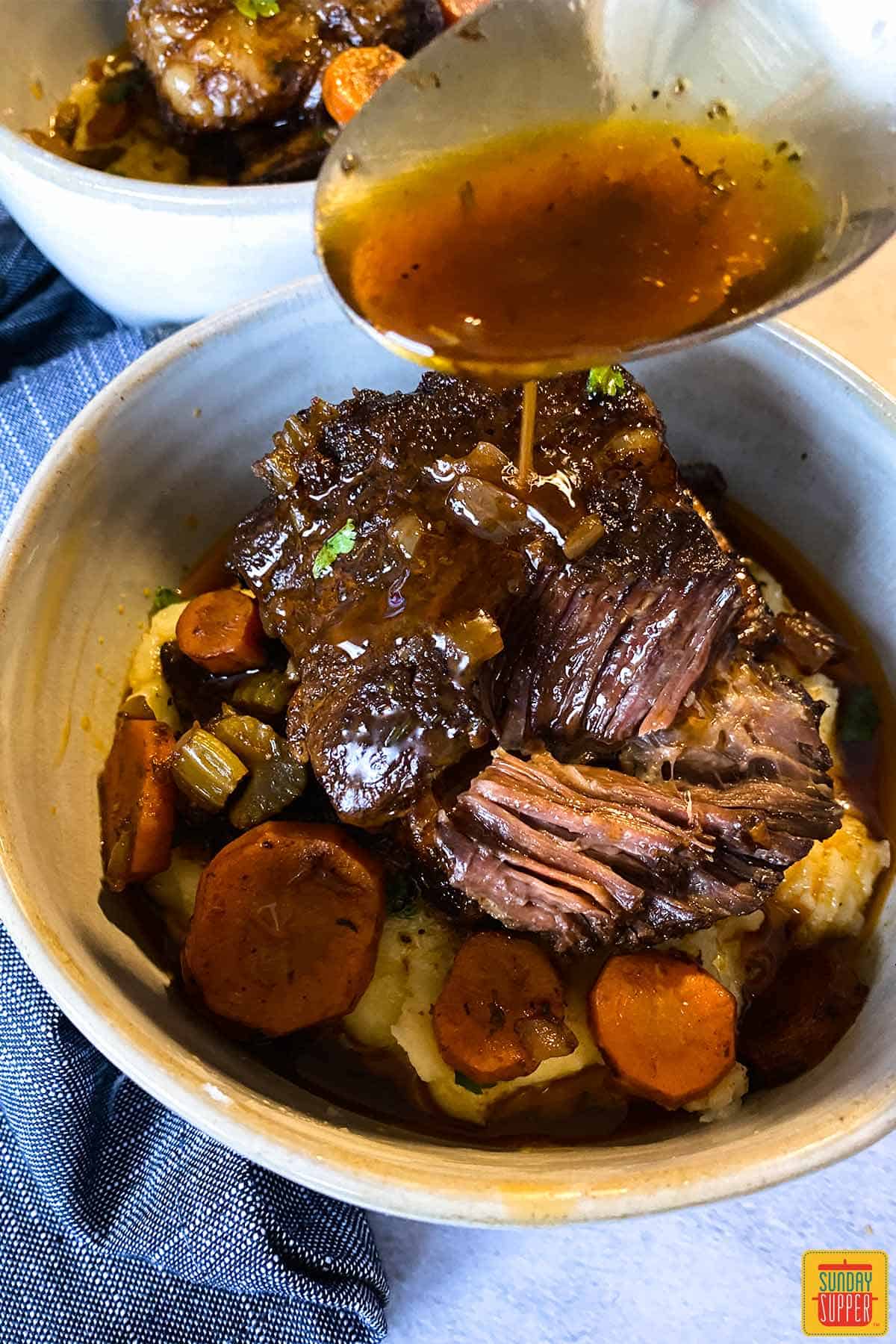 Pouring gravy on short ribs in a bowl