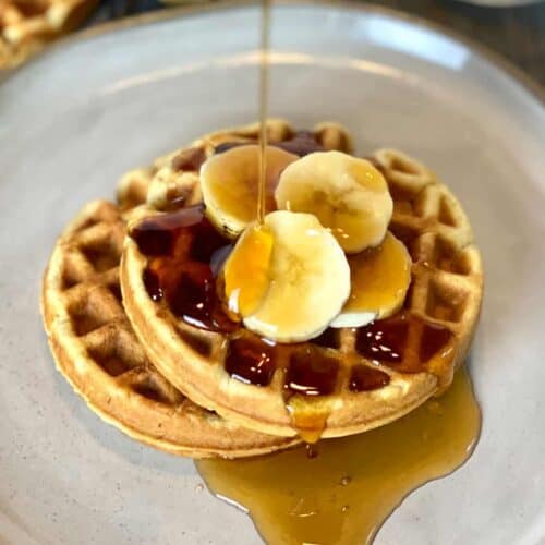 Pouring syrup onto two banana bread waffles topped with banana slices