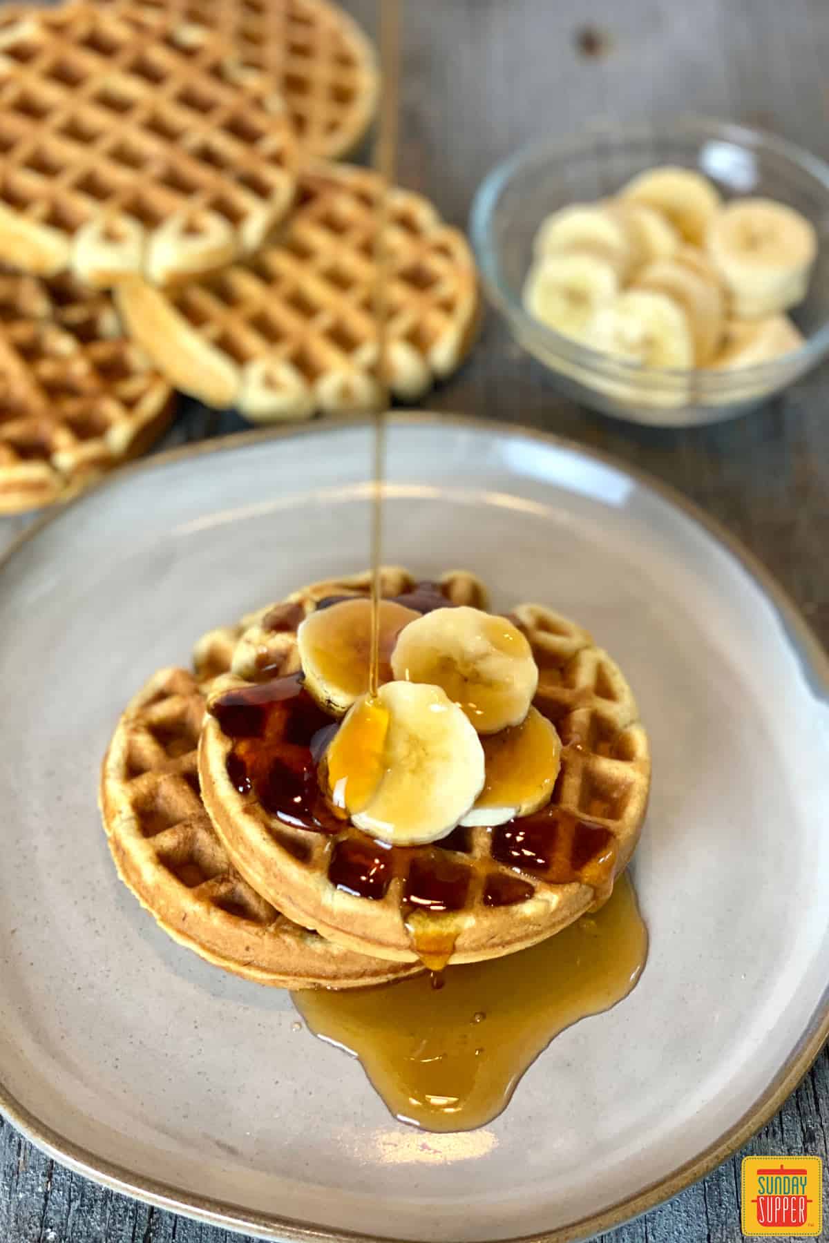 Pouring syrup onto two waffles on a plate with banana slices