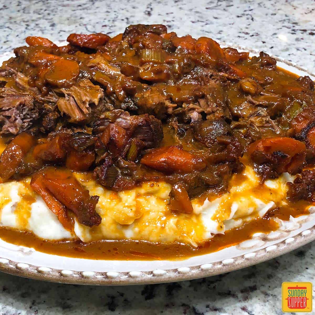 Juicy beef chuck roast over mashed potatoes on an offwhite plate