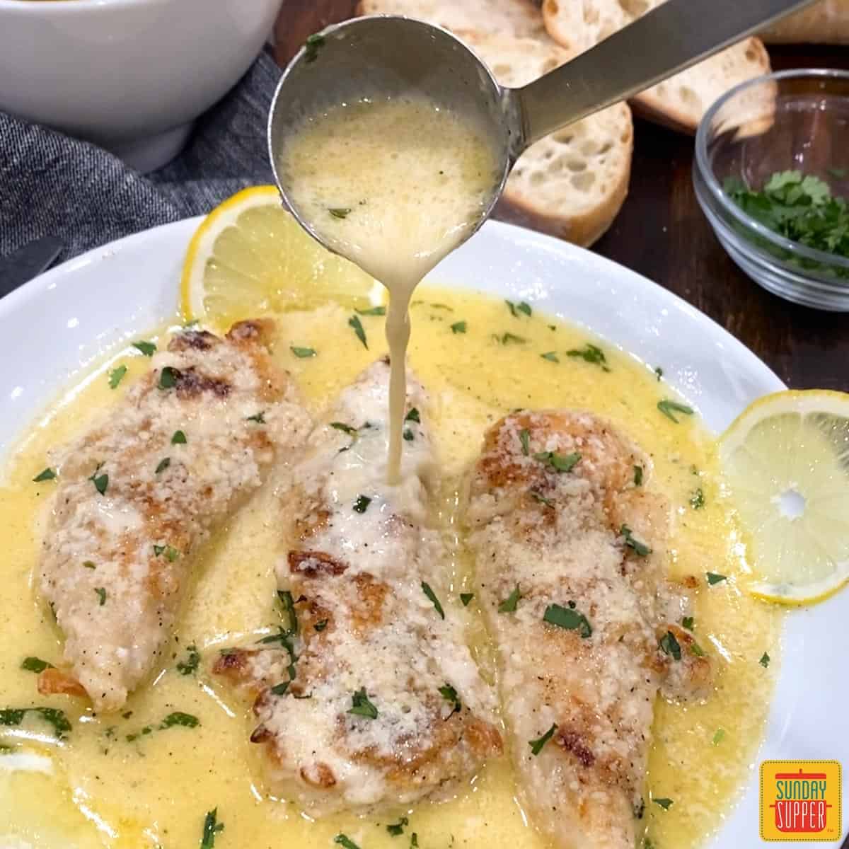 Pouring lemon butter sauce over chicken on a white plate