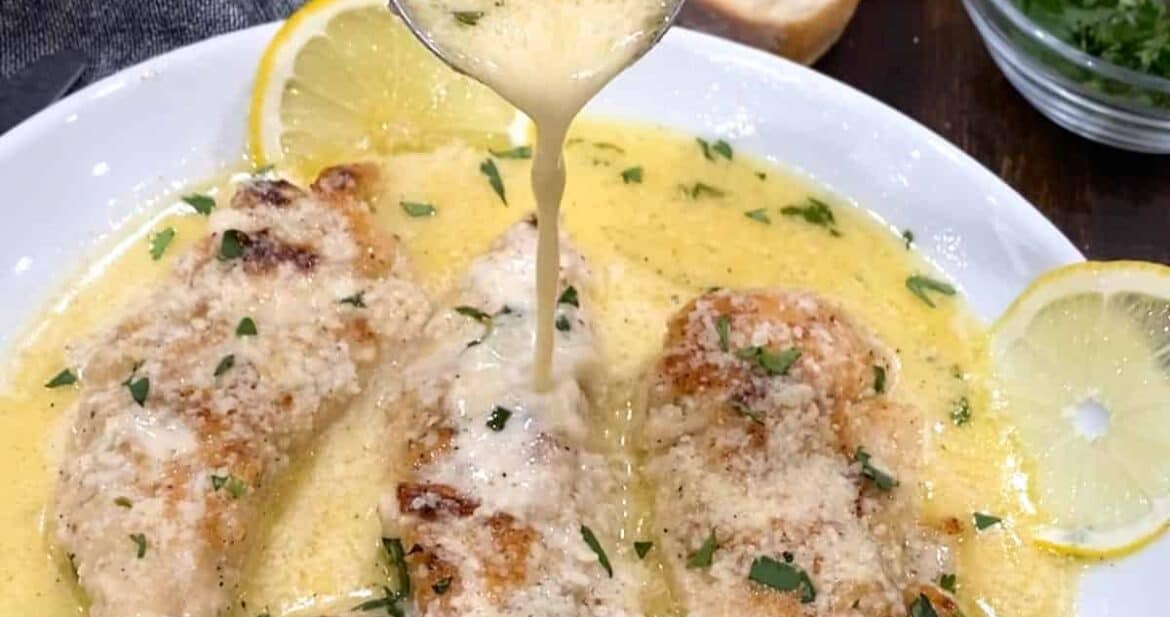 Pouring lemon garlic butter sauce over chicken on a white dish with lemon slices