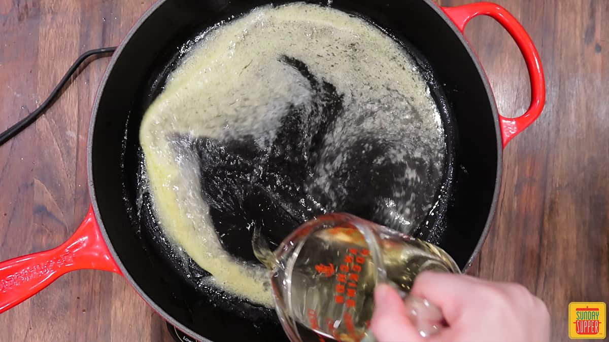 Pouring white wine into a skillet to make lemon butter sauce