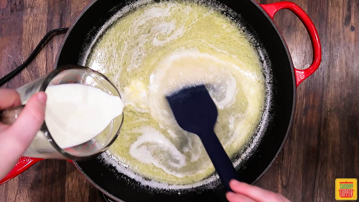 Pouring heavy cream into the skillet with lemon, butter, garlic, and white wine
