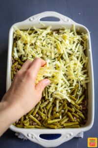 Adding grated white cheddar to casserole dish of green beans and ground beef