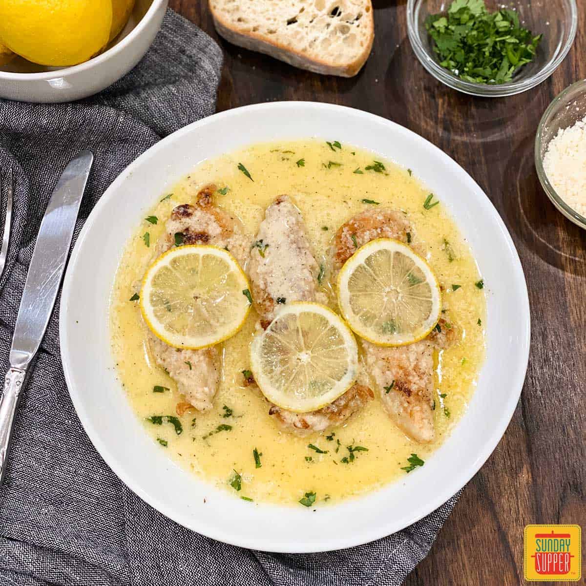 Lemon butter chicken on a white dish with three lemon slices