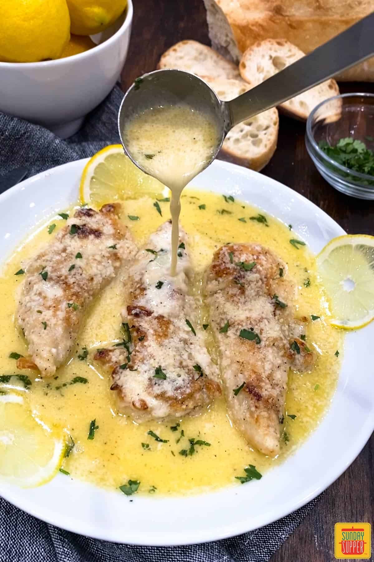 Pouring lemon butter sauce over chicken on a white dish