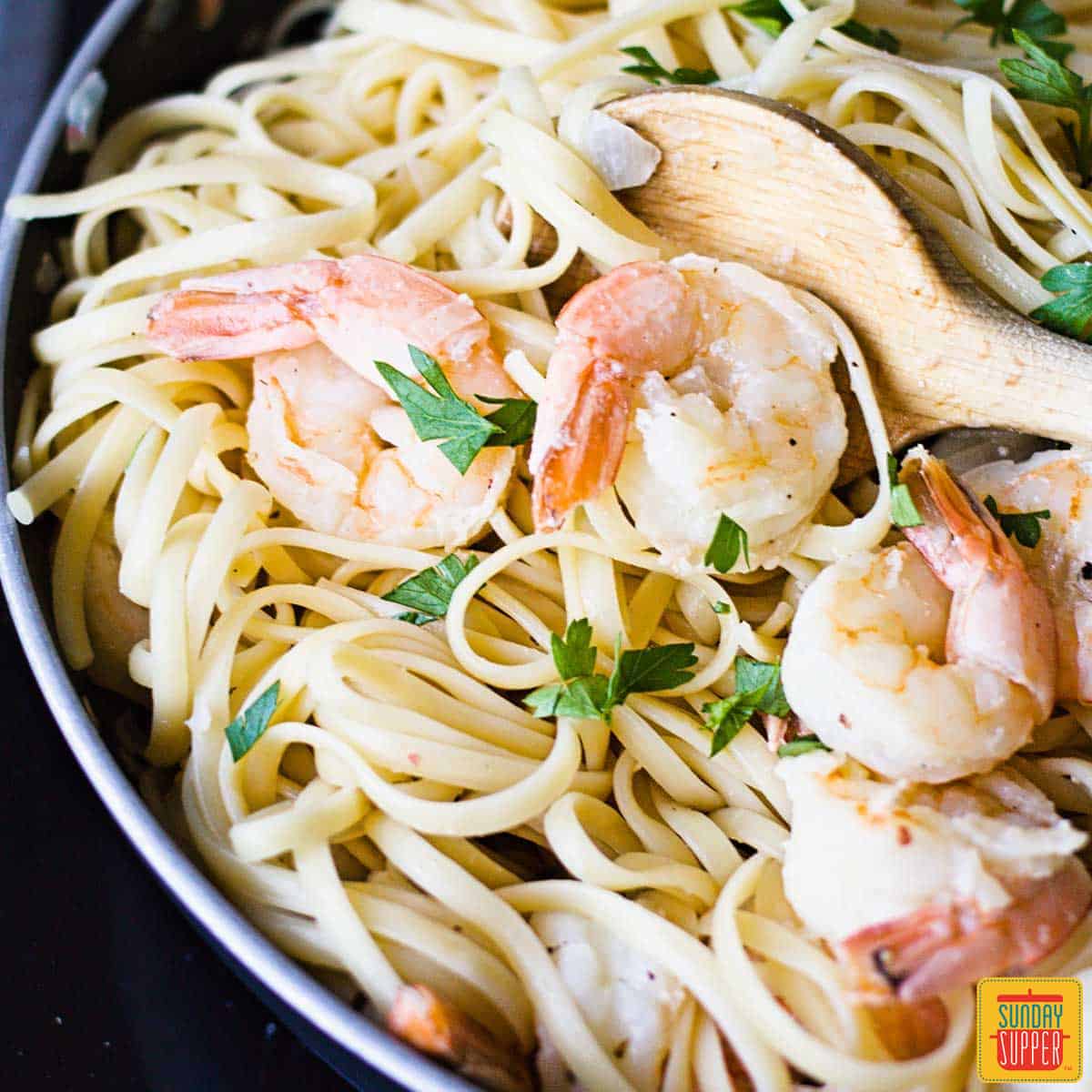 Shrimp scampi linguine in a skillet with a wooden spoon