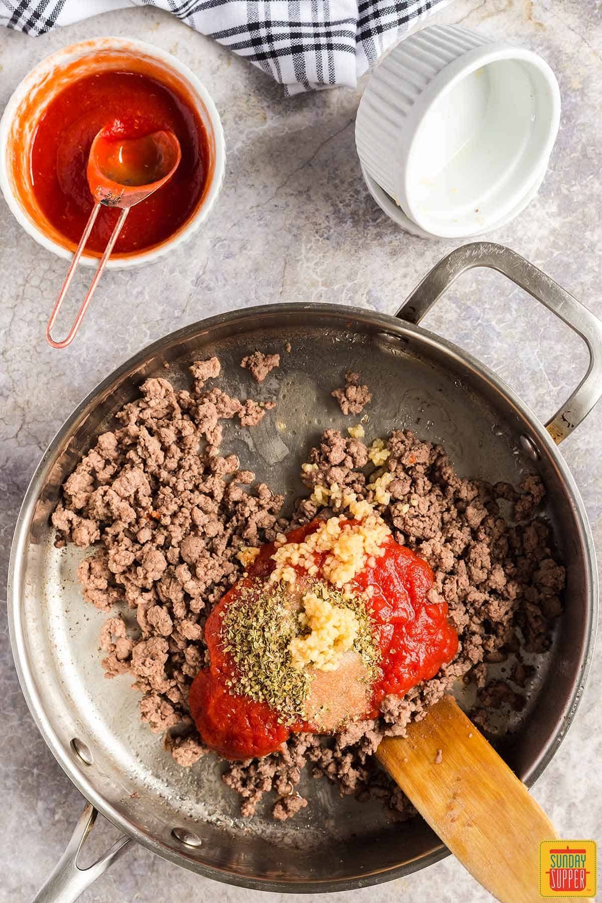 Adding tomato sauce and seasoning to ground beef in a skillet