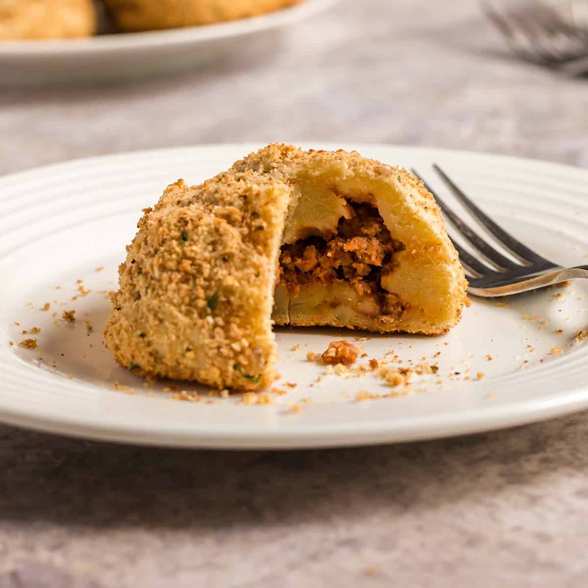 Close up of a stuffed potato ball on a plate with a bite missing