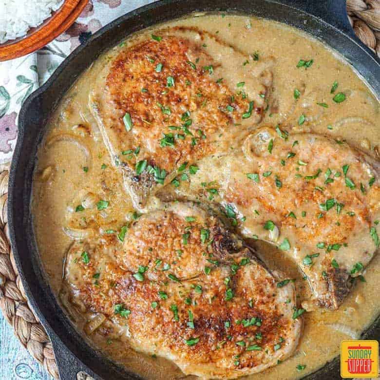 Close up of southern smothered pork chops in a black skillet for Sunday dinner ideas