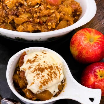 Apple crisp in two white dishes: one has ice cream on top and there are two fresh apples to the side