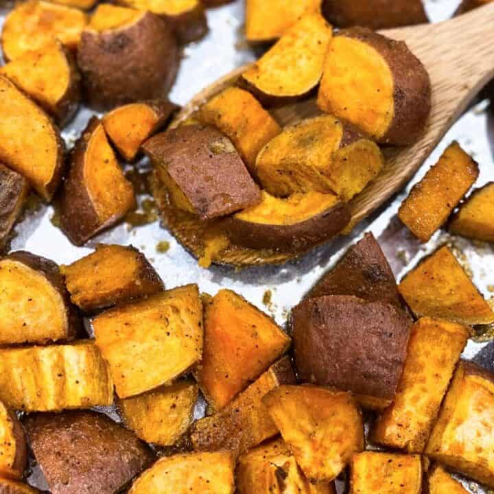 Roasted sweet potatoes with a wooden spoon on a baking sheet