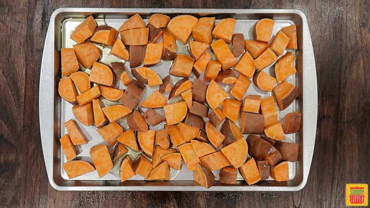 Sweet potatoes tossed with olive oil and maple syrup on a baking sheet