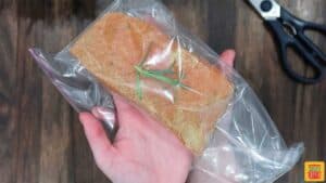 Seasoned salmon in a plastic bag with a rosemary sprig on top