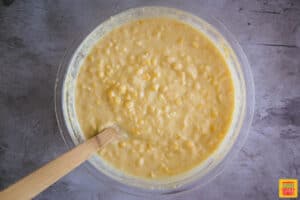 creamed corn casserole mix in a glass bowl with a wooden spoon