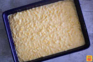 Creamed corn casserole spread out into a blue baking dish unbaked