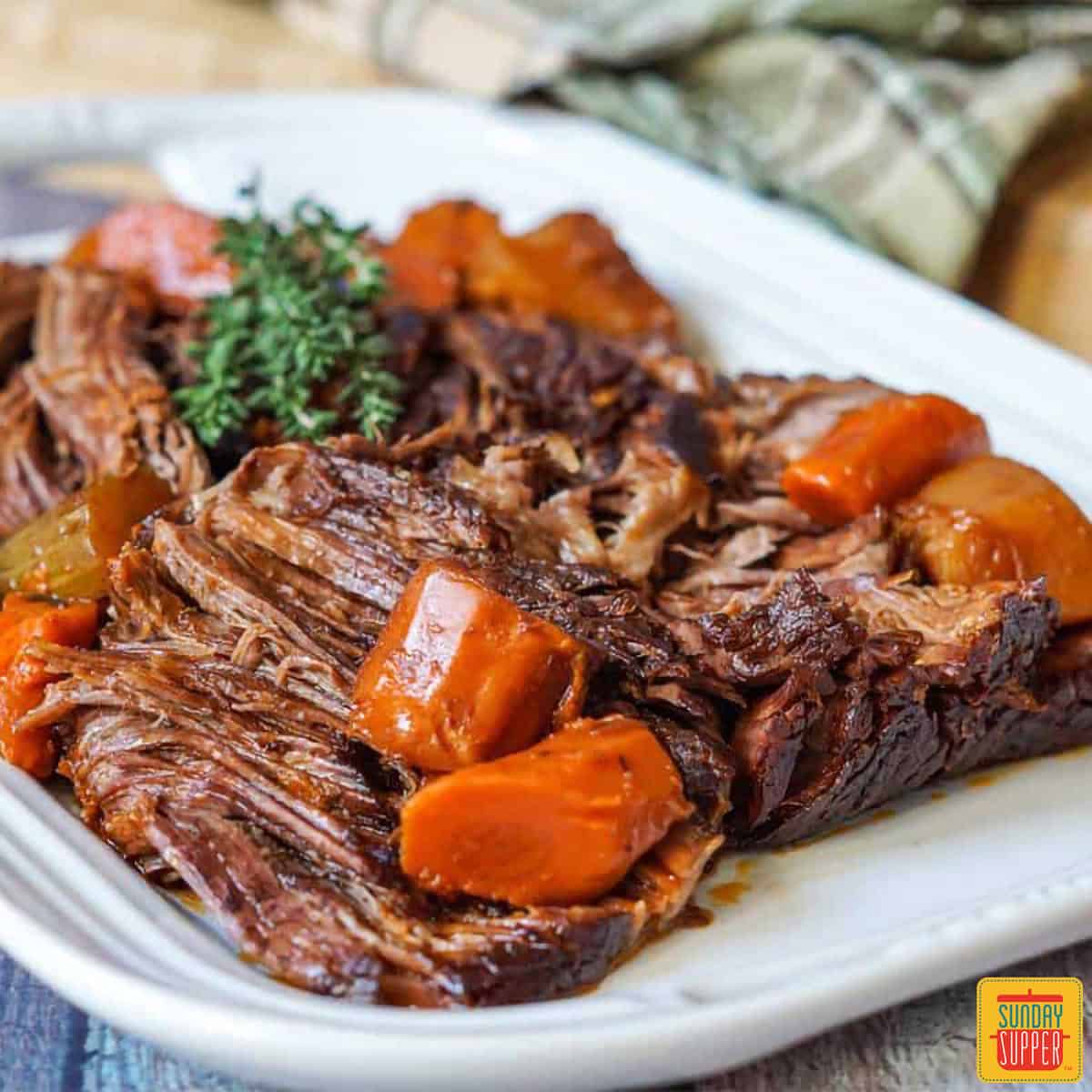 Beef chuck roast on a white plate with carrots and herbs