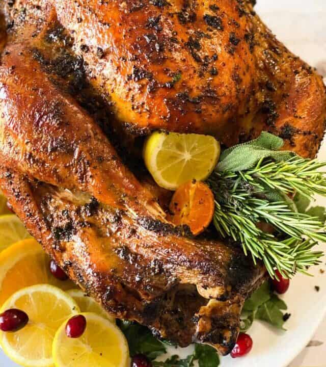 Close up of turkey on a platter with citrus, herbs, and cranberries