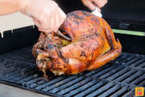 Lifting a cooked turkey off the grill using two serving forks