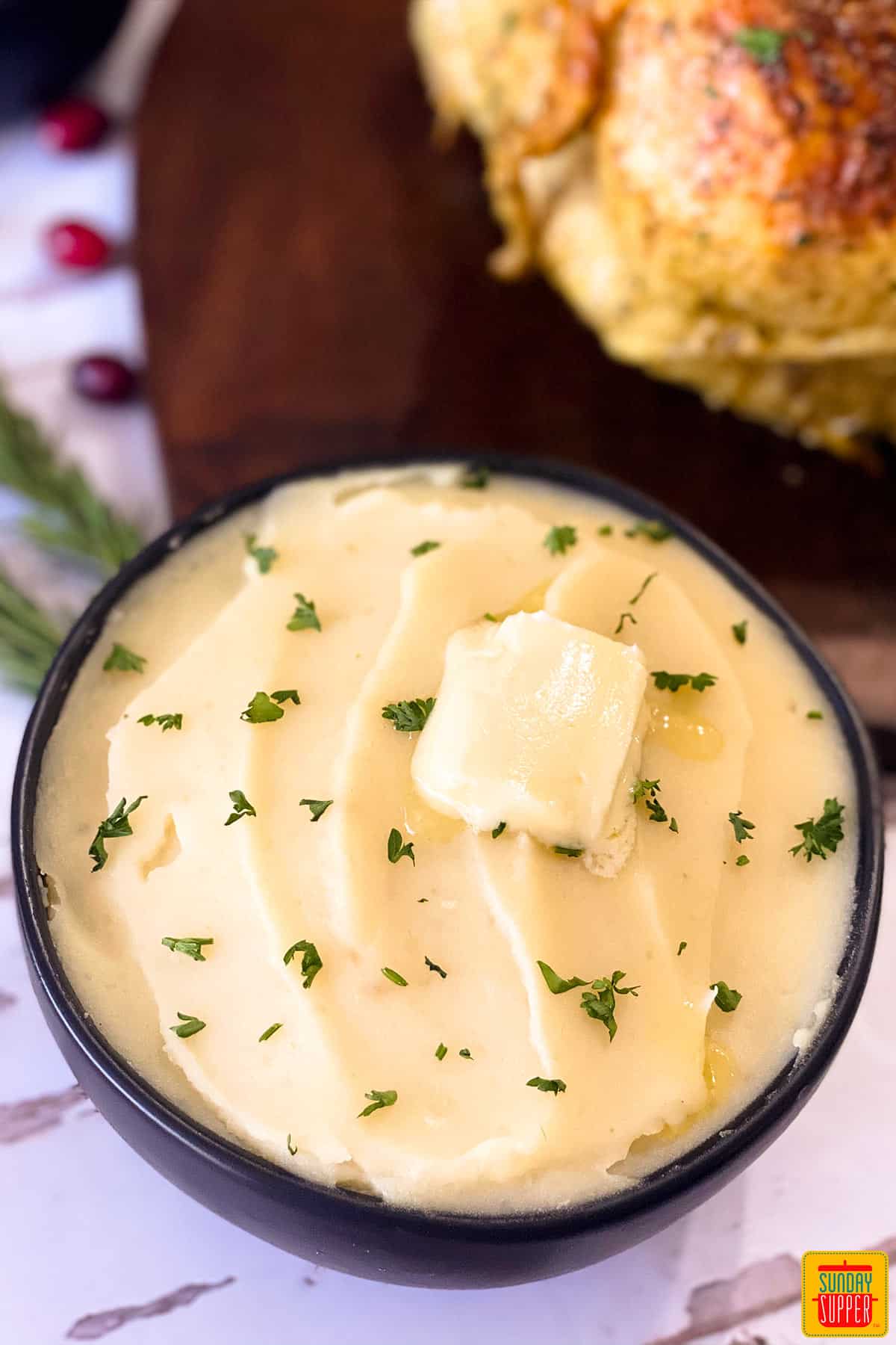 A bowl of mashed potatoes with a pat of butter on top next to turkey on a cutting board