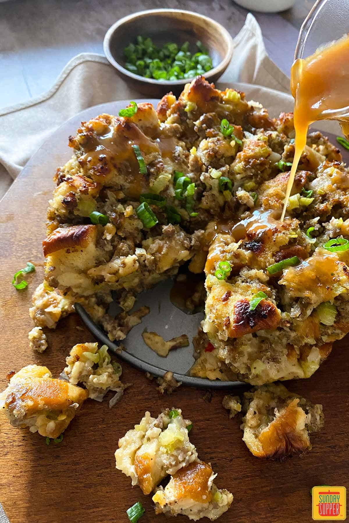 Pouring gravy over instant pot stuffing on a wooden board
