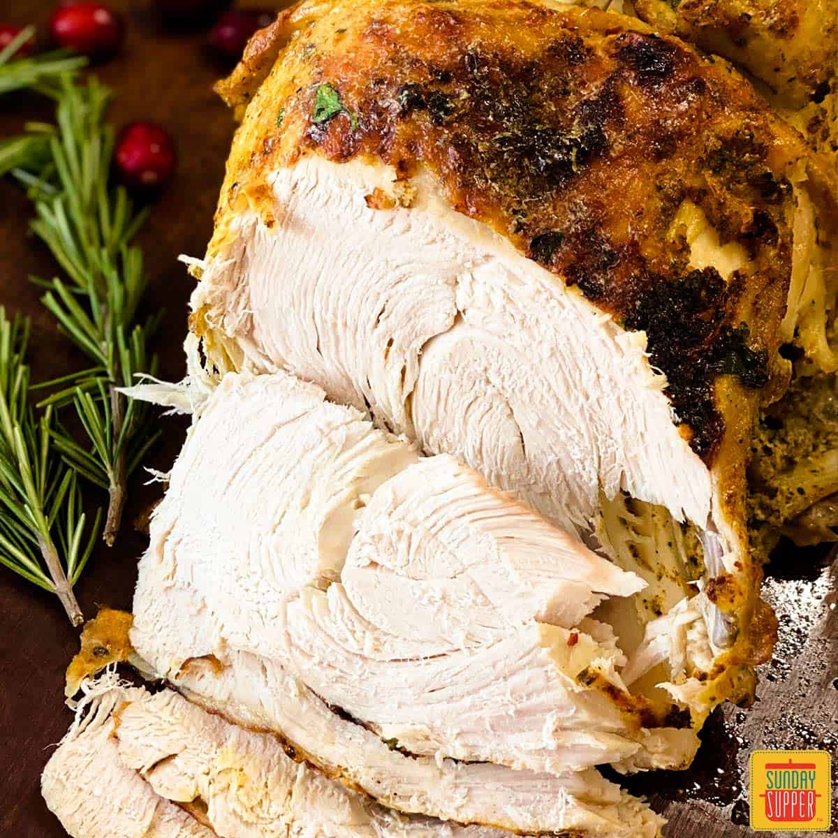 Sliced Instant Pot Turkey Breast next to sprigs of rosemary and cranberries on a cutting board