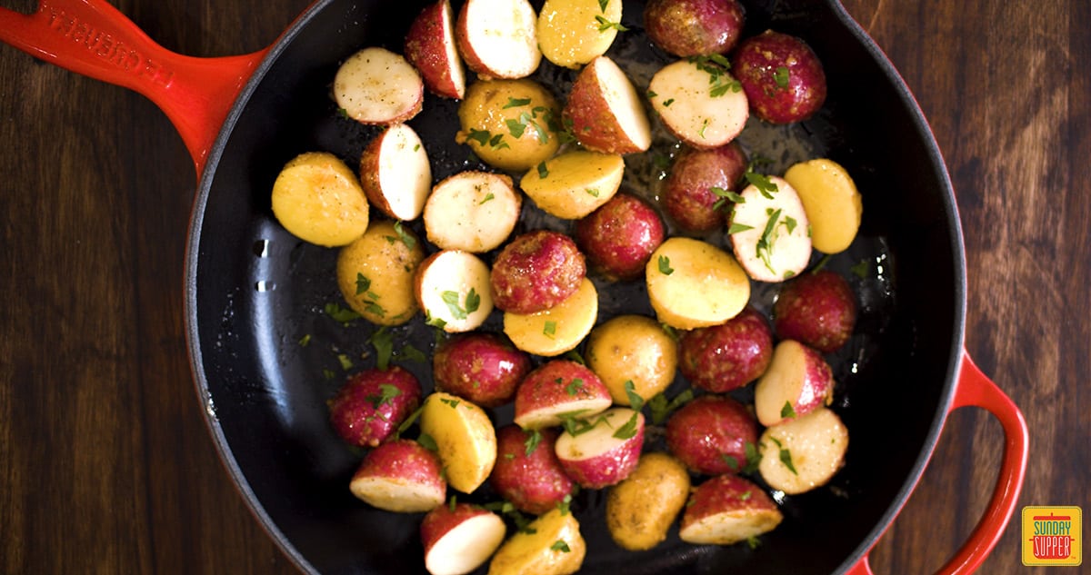 Uncooked small potatoes in a skillet with seasoning and parsley