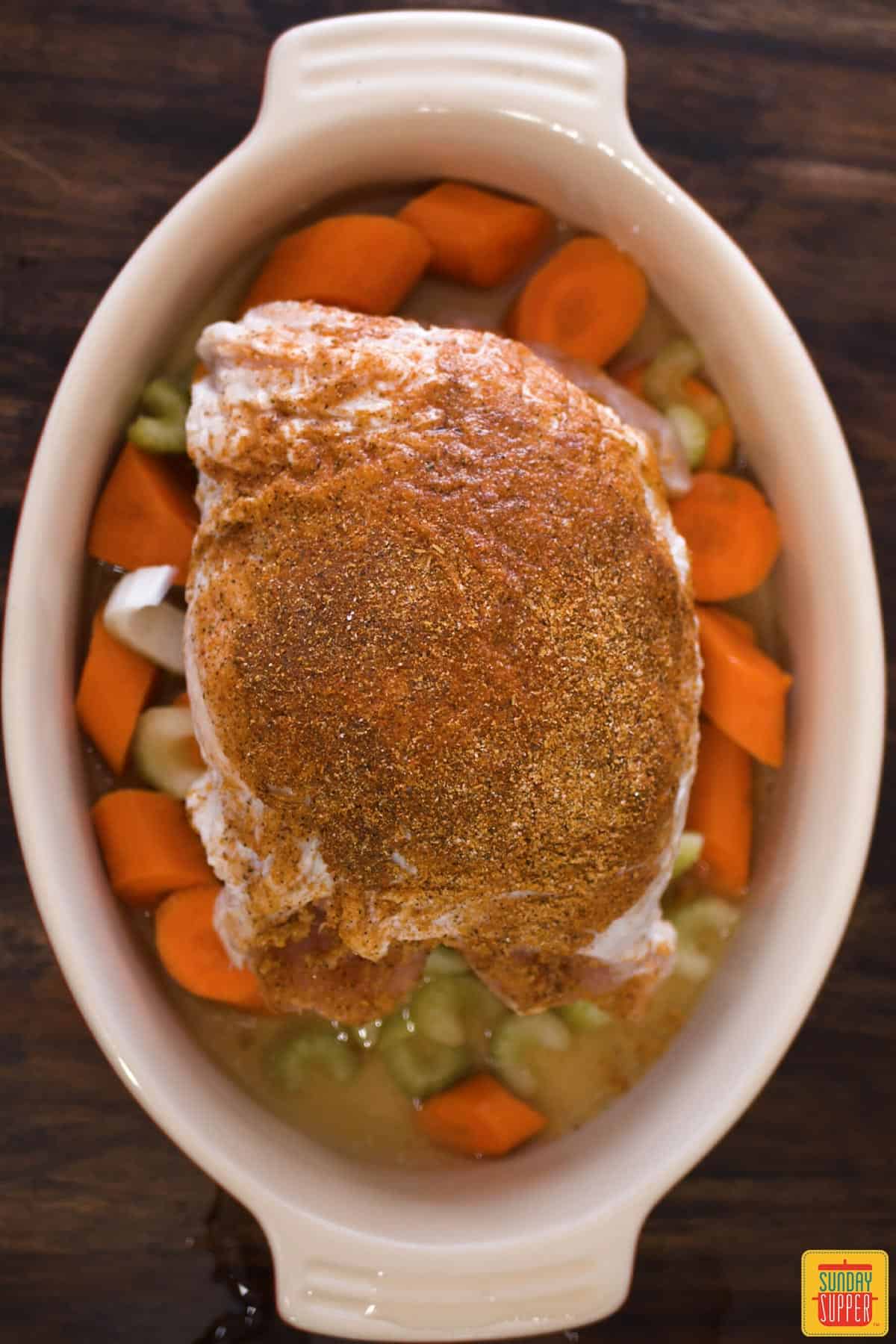 Turkey covered in rub in a dutch oven over vegetables