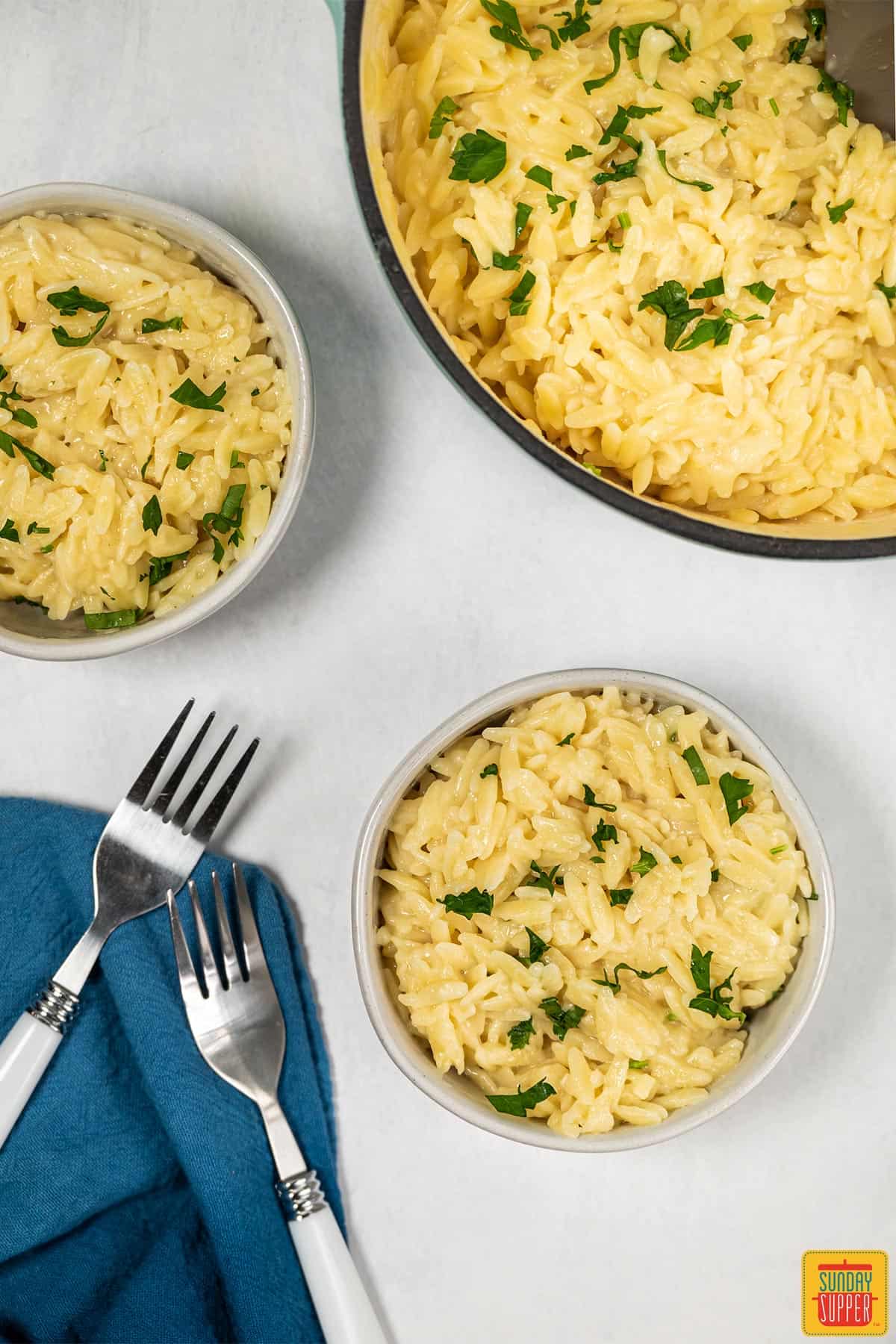 Two bowls of cheesy orzo risotto with a pot of risotto