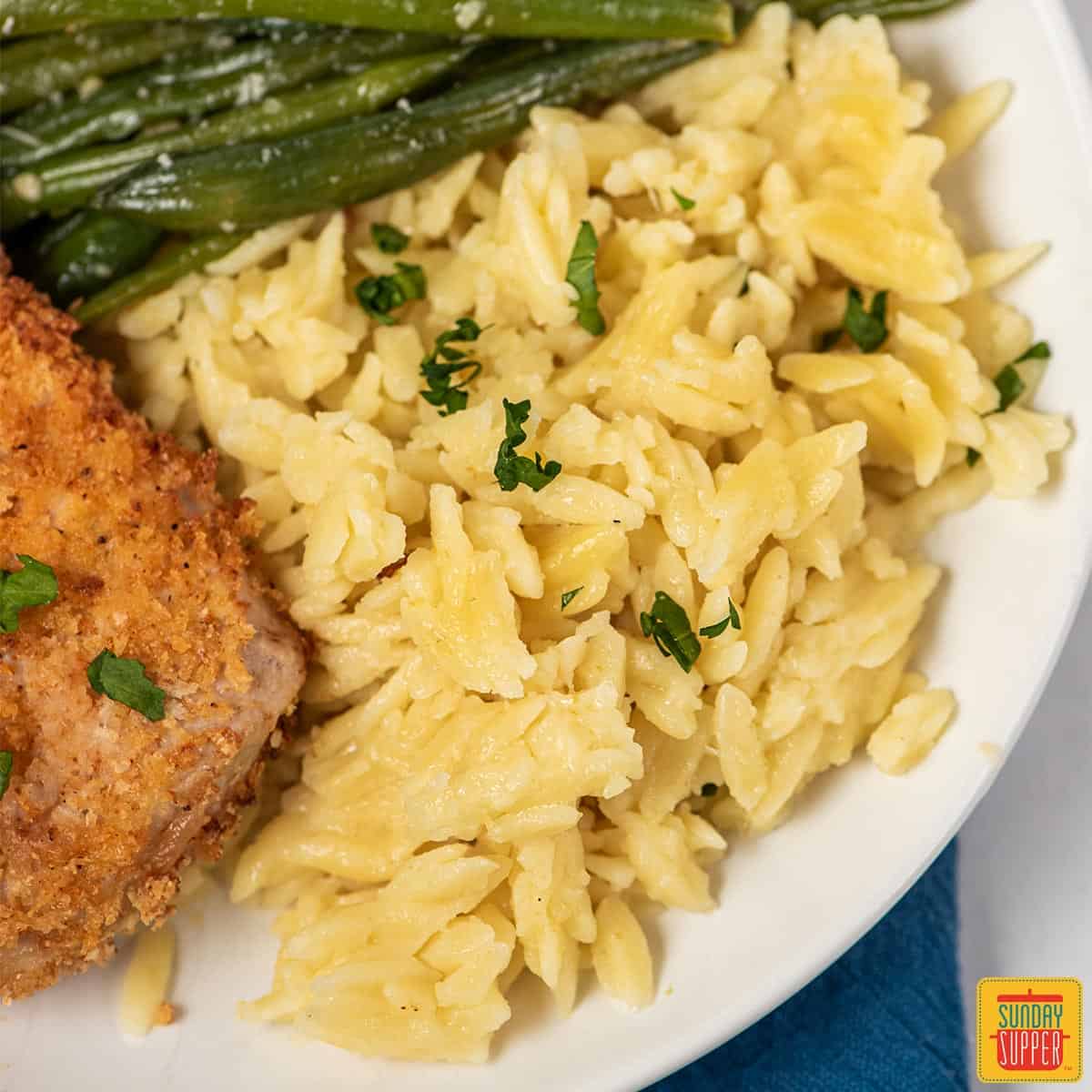 Cheesy orzo risotto on a plate with green beans and air fryer pork chops