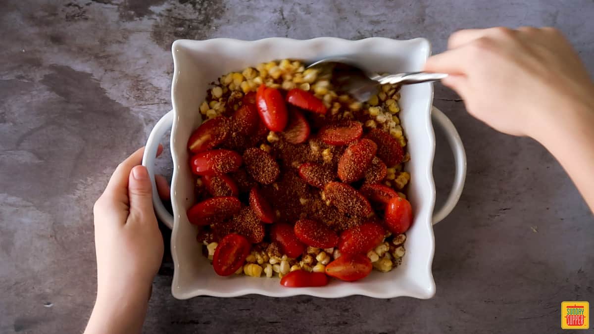 Mixing corn and tomatoes with seasoning in a white baking dish