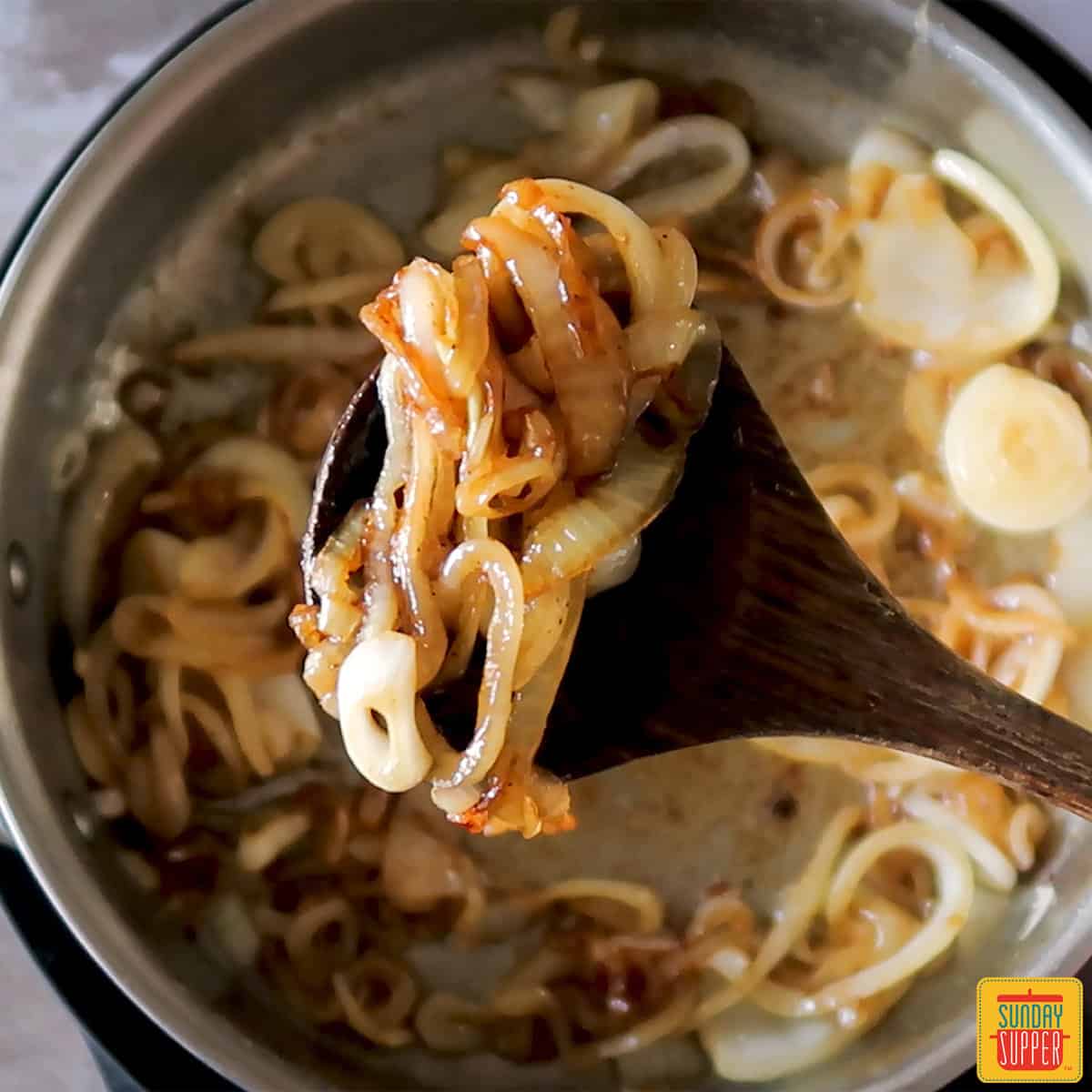 caramelized onions on a wooden spoon over top a pan of onions